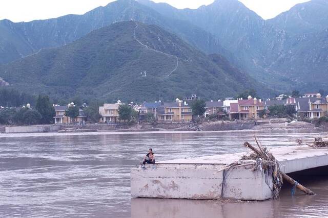 8月4日，村民坐在拒马河的一个断桥上眺望对岸的村庄。新京报记者曹晶瑞摄