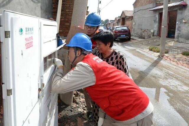 电力工作人员正在帮助庞嘴村村民检查供电线路。（新华社发）