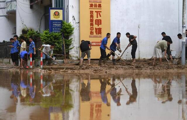 8月24日，在广西百色市凌云县下甲镇，人们在清理道路上的淤泥。新华社记者陆波岸摄