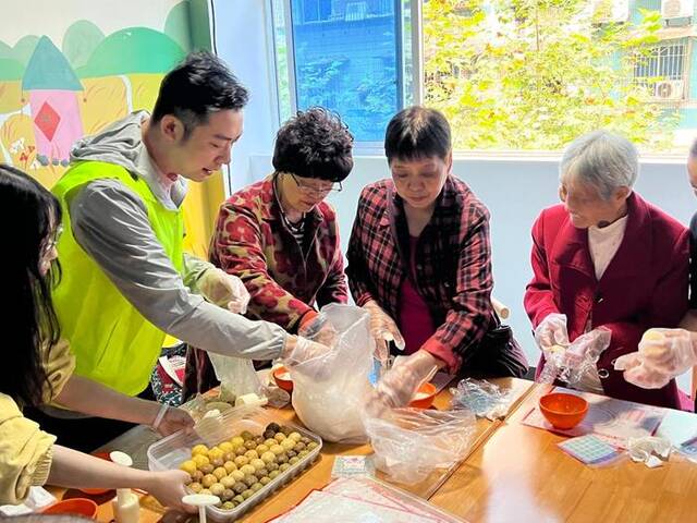 9月28日，老人们与工作人员在重庆市渝北区双龙湖街道老年餐中央厨房制作手工月饼。新华社记者赵佳乐摄