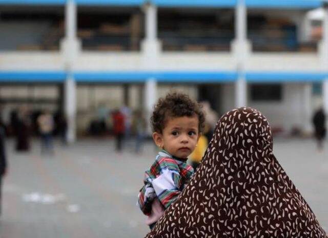 10月9日，一名妇女抱着小孩在加沙地带南部城市汗尤尼斯的一所学校躲避以色列空袭/图源：新华社