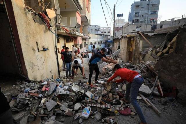 11月3日，在加沙地带南部城市汗尤尼斯，人们清理遭以色列袭击后的建筑废墟。新华社发（亚西尔·库迪摄）