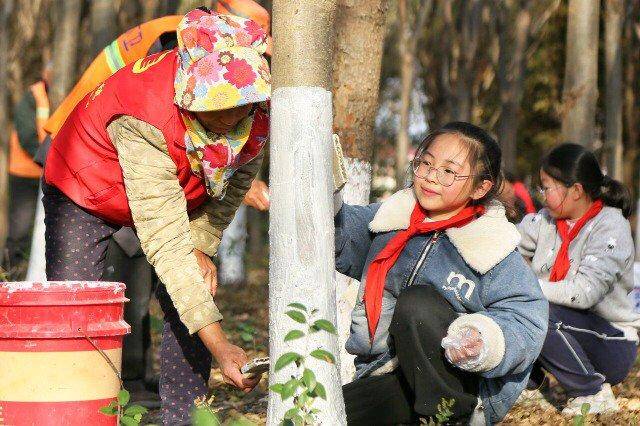 小学生们在保洁员和志愿者的指导下对树木进行涂白。通讯员周强摄