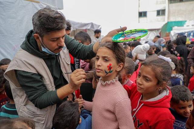 12月7日，在加沙地带南部城市拉法的一处临时庇护所内，志愿者和儿童进行互动。新华社发（里泽克·阿卜杜勒贾瓦德摄）
