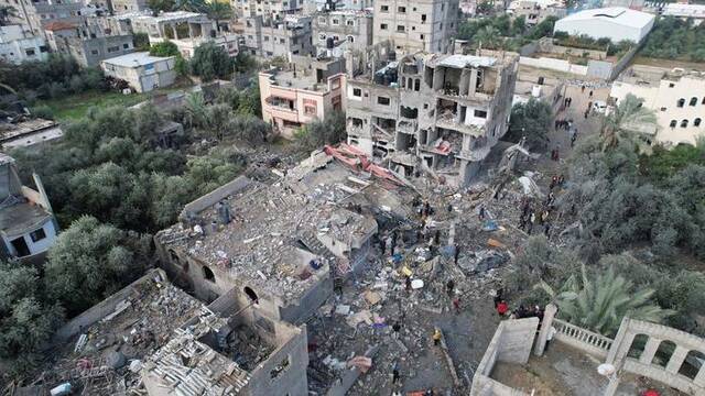 12月25日，加沙中部迈加齐难民营遭到以军空袭后，巴勒斯坦民众聚集在受损建筑附近图源：ICphoto