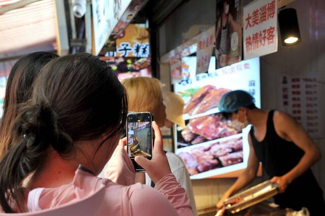 ▲今年6月，“鸭头小哥”在店里忙碌时有顾客拍照围观。图据视觉中国