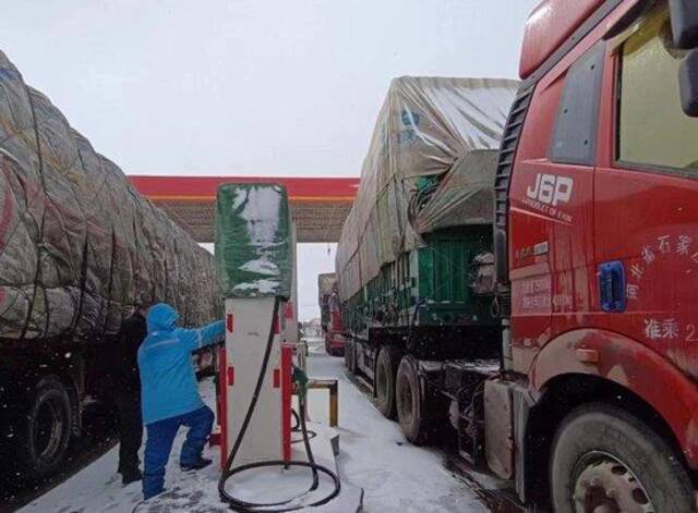 图为员工顶风冒雪为车辆加油。