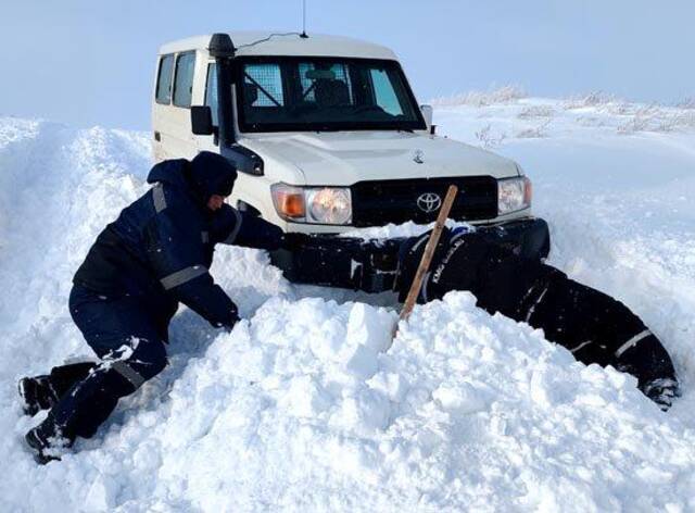 施工车辆在积雪路段被困，司机和查线工挖雪救车。