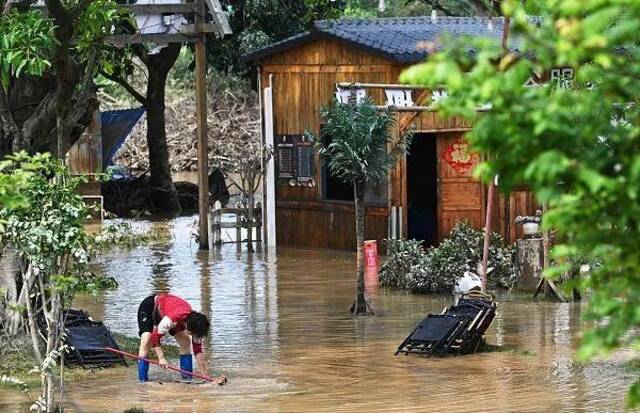 2024年4月24日，广东清远，暴雨过后，一名妇女在泥泞的水中捡椅子。（图