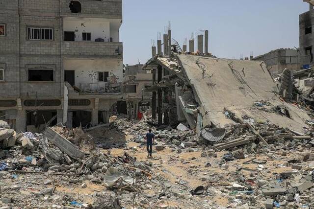 5月21日，在加沙地带南部城市汗尤尼斯，巴勒斯坦人经过以军轰炸后的废墟。（新华社发里泽克·阿卜杜勒贾瓦德摄）