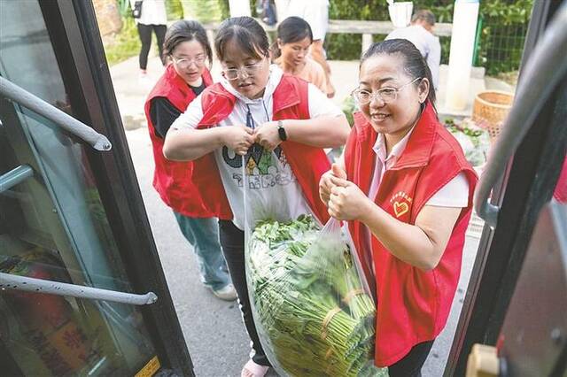 近日，在新湾村招呼站，志愿者帮助菜农把菜搬运到公交车上。新华社记者陈思汗摄