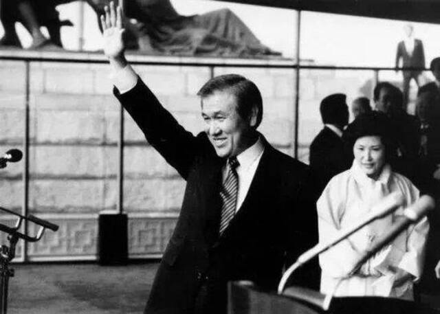 ·1988年2月25日，就任韩国第13届总统的卢泰愚在就职仪式上向与会者们举手示意。后面是他的夫人金玉淑，卢素英的母亲。