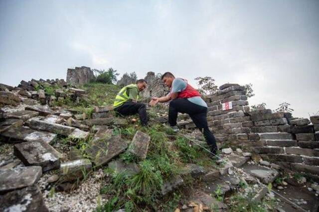 技工杨战杰（右）在指导工人拉线划设北京箭扣长城研究性修缮考古发掘范围（2022年8月17日摄）。新华社记者陈钟昊摄