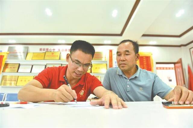 百坭村村“两委”办公室，34岁的驻村第一书记农俊海(左)为村民办事。新华社记者黄孝邦摄