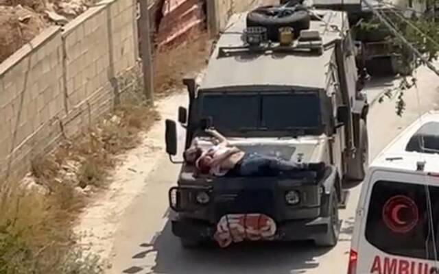 图为当地时间22日，以军将一名受伤的巴勒斯坦男子绑在一辆军用吉普车的引擎盖上带走图源：社交媒体X上流传的视频截图