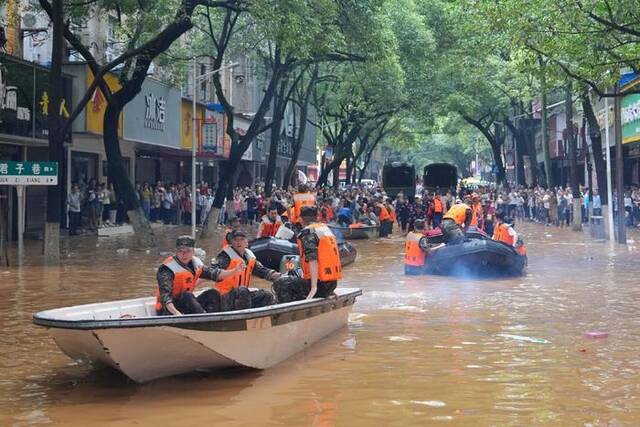 2024年7月2日，湖南平江县，救援人员乘坐冲锋舟前往受灾地区，身后站着广大的市民群众。中新社记者杨华峰/视觉中国图