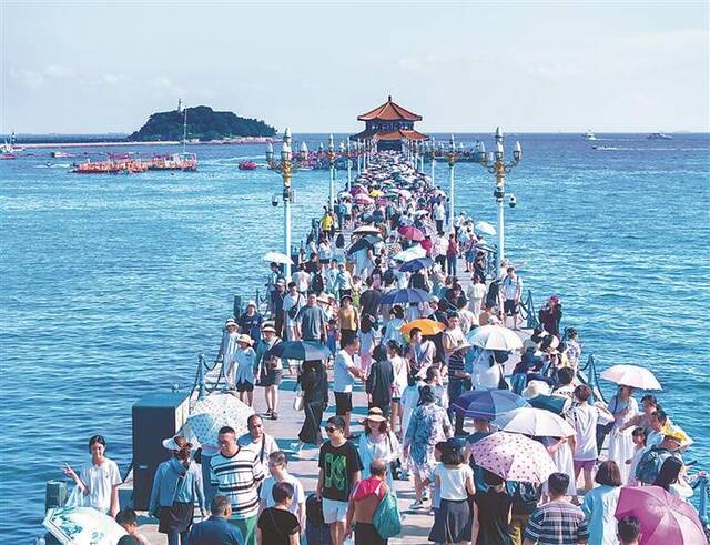 图为近日，大批市民和游客来到青岛的标志性景点栈桥景区游玩。